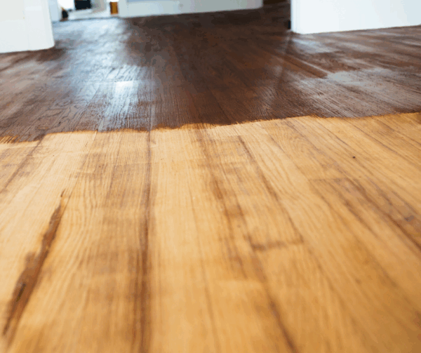 Close-up view of a refinished wooden floor showing distinct areas of sheen and finish.